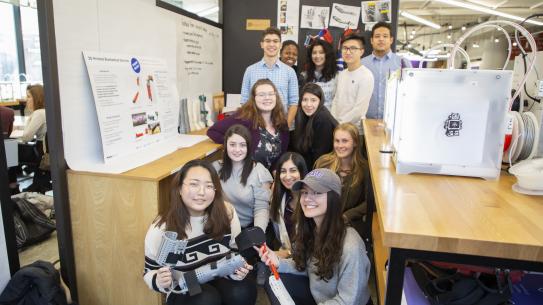 a team of students in the MakerSpace with a student holding their MakerBrace project