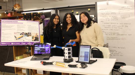 Team standing in front of poster and behind a table with a presentation and prototype