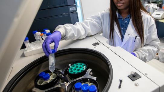 a young Black woman in lab gear placing a tube in machine