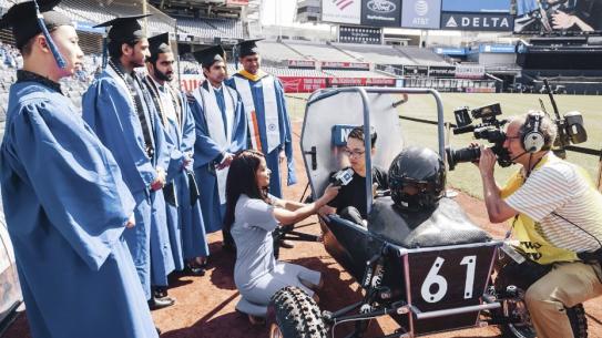 Graduating student interviewed at Yankee Stadium, sitting in car