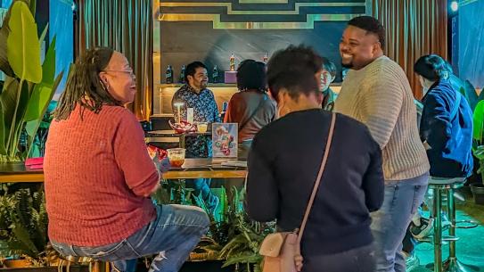 Small group of attendees chatting near a game station with colorful decor.