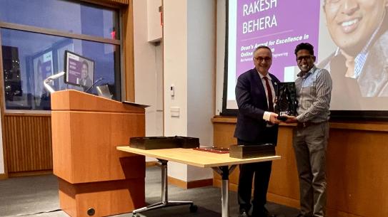 Two people stand, posed, smiling while holding a boxed glass trophy