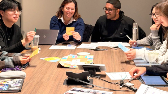 a group of smiling students sitting around a large table working on a project together