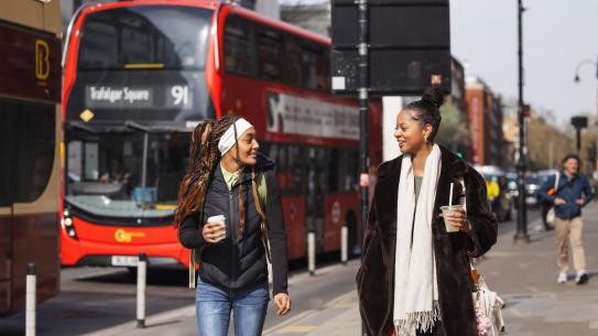 2 students walking in London with a double-decker bus in the background