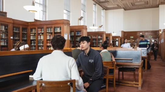 Students studying in library with wood shelving and furniture
