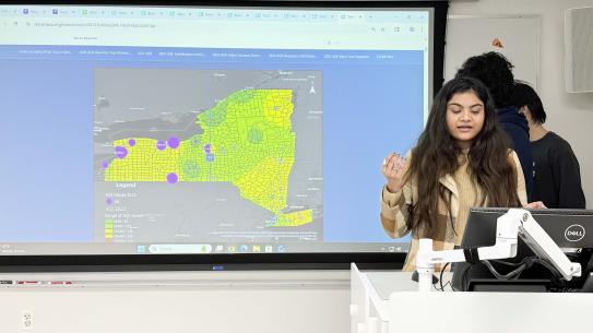 Srishti Ananya, Krishna Talluri, and Tianze Liu speaking in front of a map of New York.
