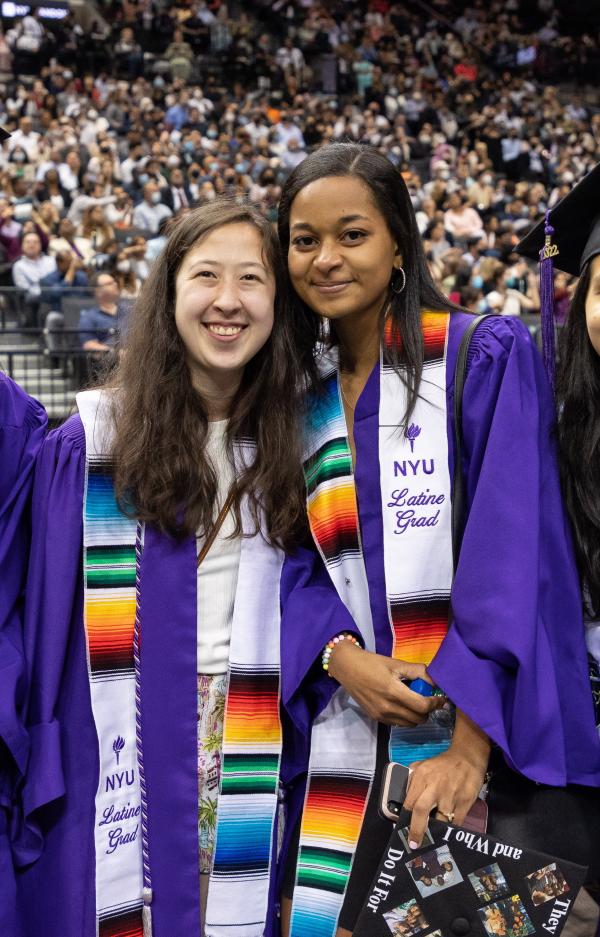 two female graduates in robes with "Latine Grad" sashes