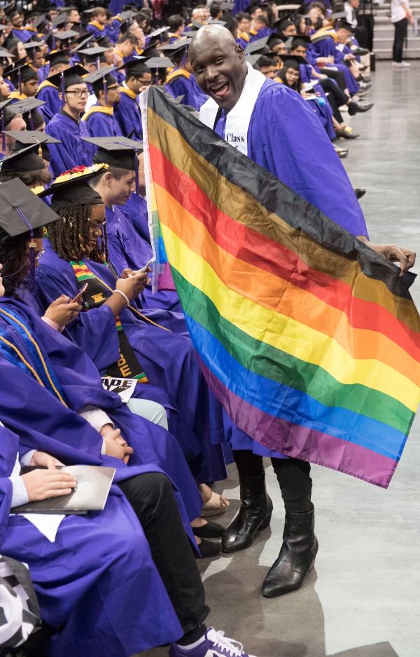 a graduate holding a rainbow flag at commencement