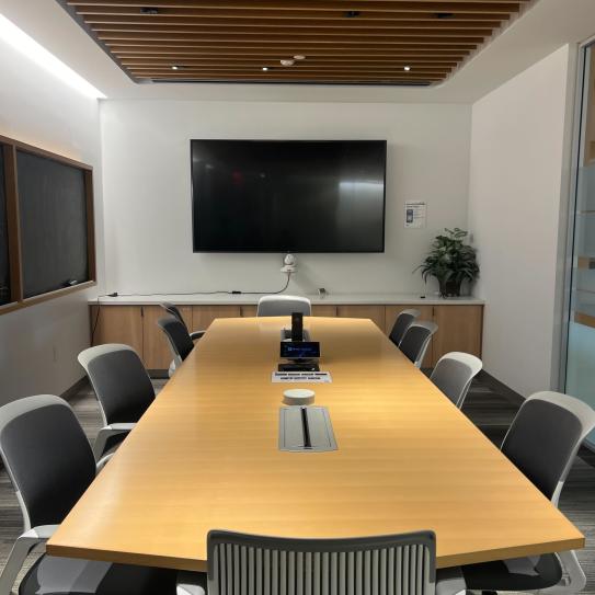 Room with a conference table with 10 chairs and a display.