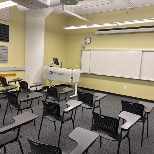 In the foreground, three rows of chairs with tablet arms. The chairs face a whiteboard, a lectern, and a projector screen.