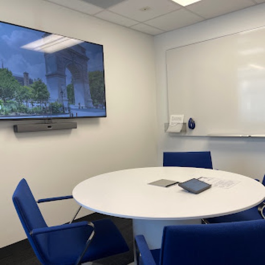 A small room with a round table with four chairs, a whiteboard, and a display on the wall.