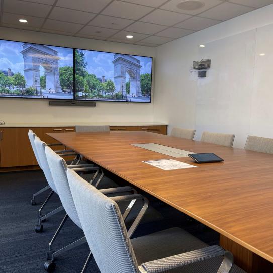 A room with a conference table with 10 chairs. At one end of the table there are two large displays.