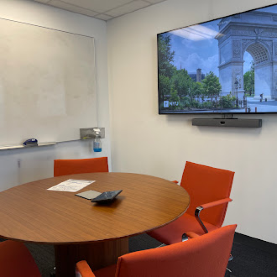 A small room with a round table with four chairs, a whiteboard, and a display on the wall.