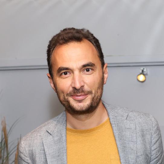 Man with cropped beard, short hair in a yellow shirt and grey jacket