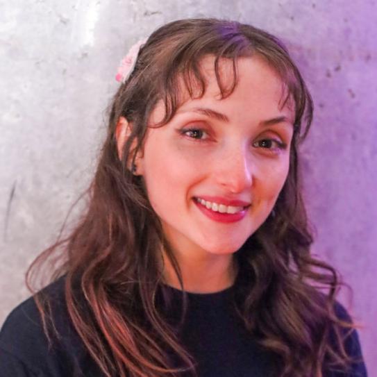 A smiling white woman with long brown hair, brown eyes, face tilted towards the viewer's right.