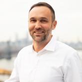 Man with cropped beard, short hair in a white shirt.