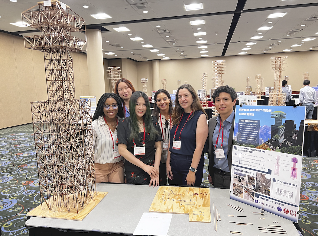  NYU Tandon Seismic Design Team members behind a table and a human size wood stick structure