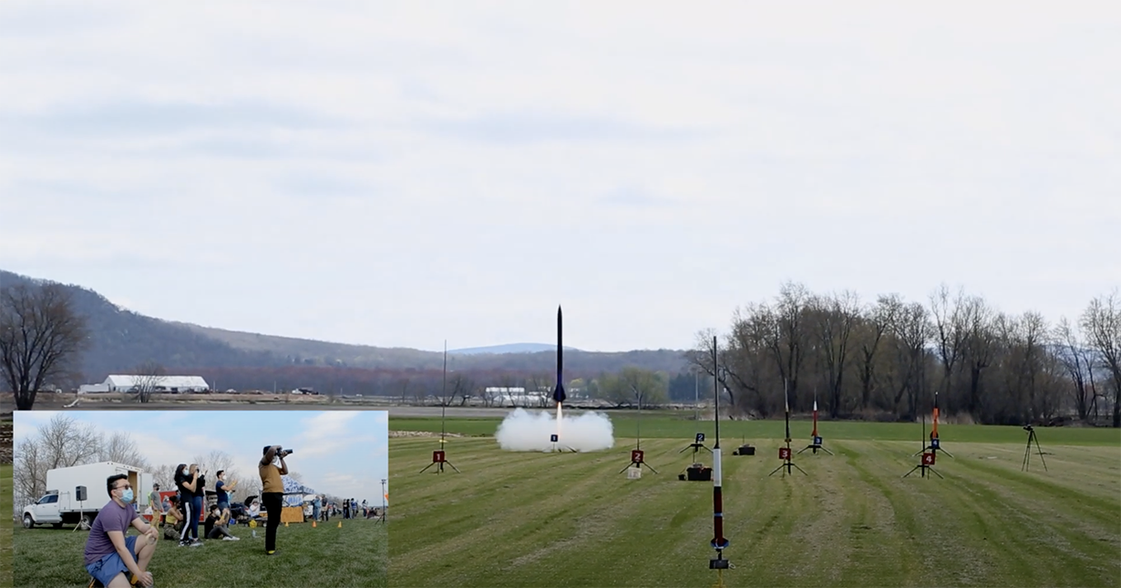 Students watch as a rocket takes flight in an empty field.